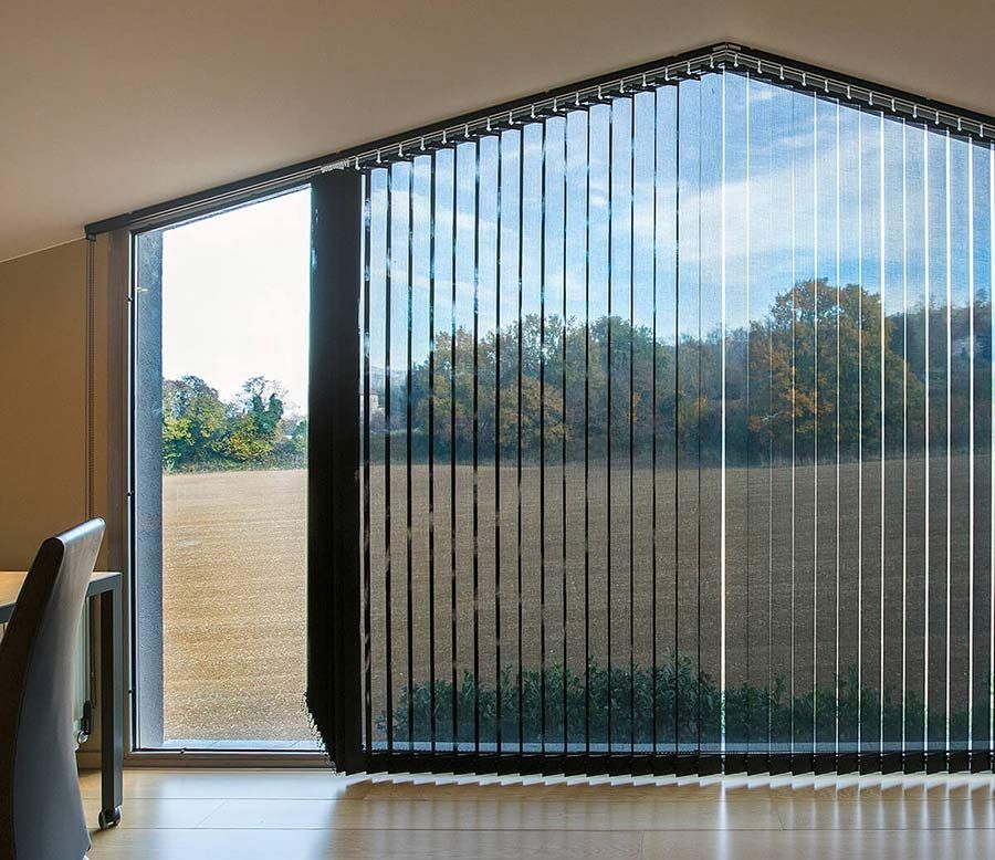 Persianas verticales negras en una ventana grande y en ángulo con vista a un campo y árboles.