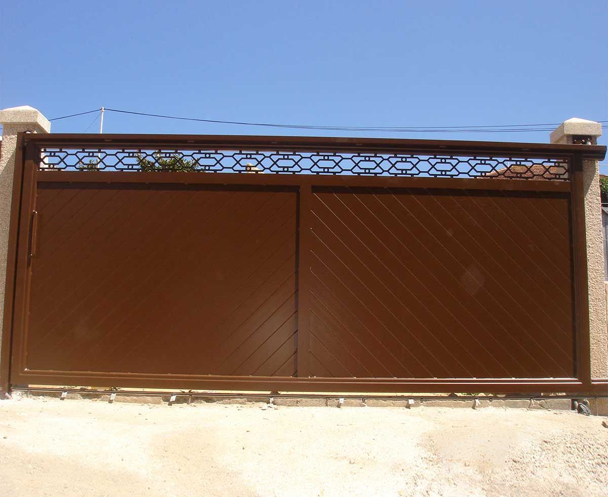 Puerta corrediza de metal marrón con sección superior decorativa, contra un cielo azul.