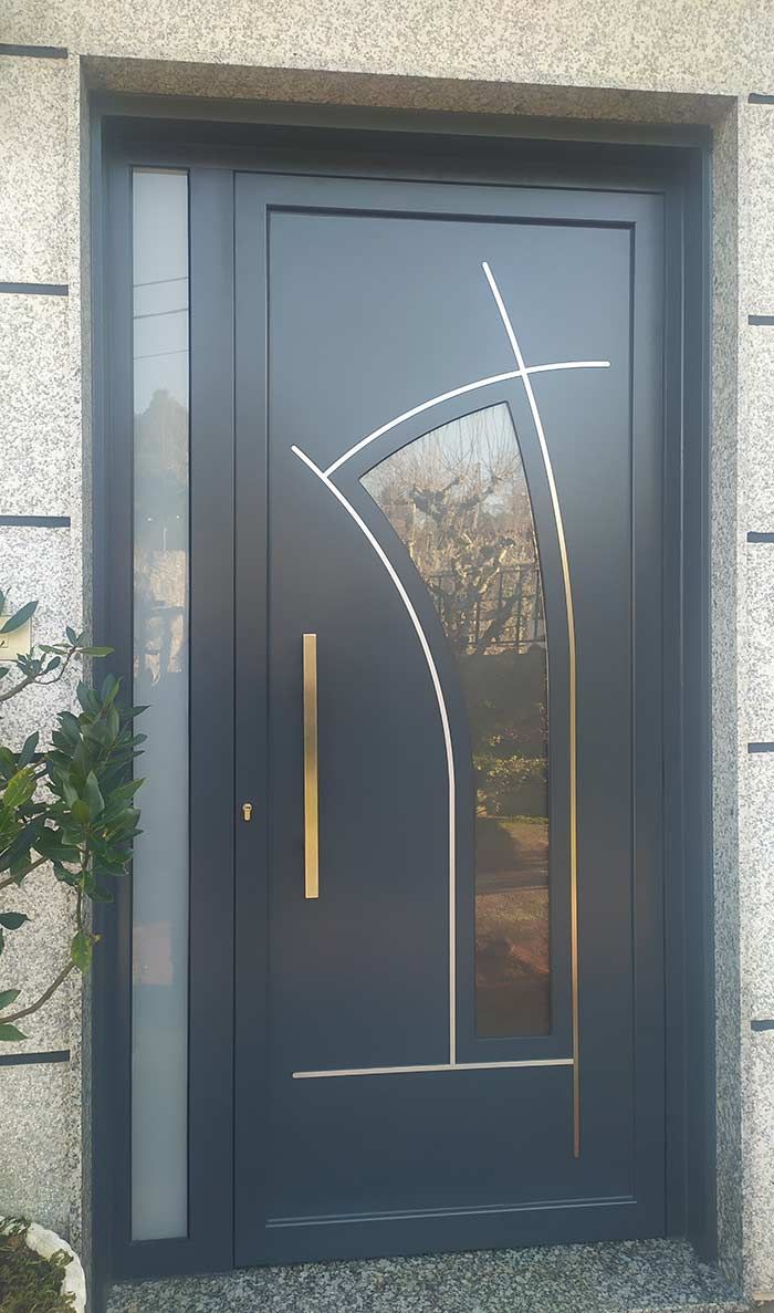 Puerta de entrada color gris oscuro con panel de vidrio y manija dorada engastada en pared de granito.