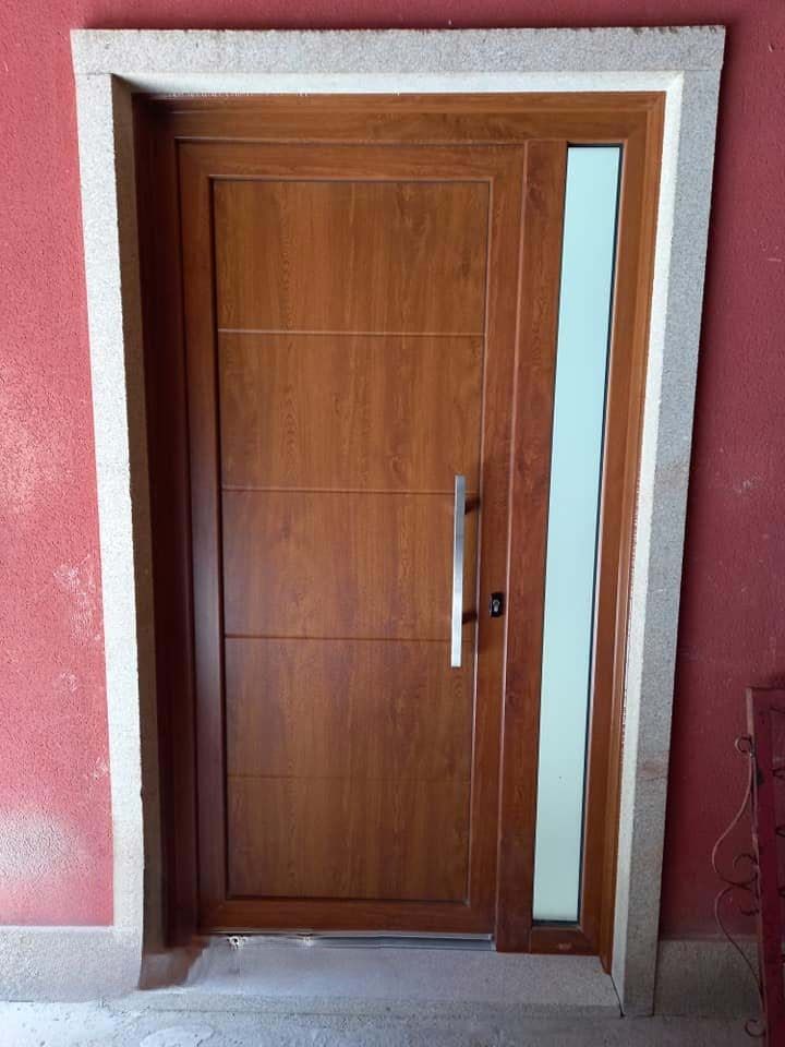 Puerta de entrada marrón con ventanal, colocada en un marco de piedra sobre una pared roja.