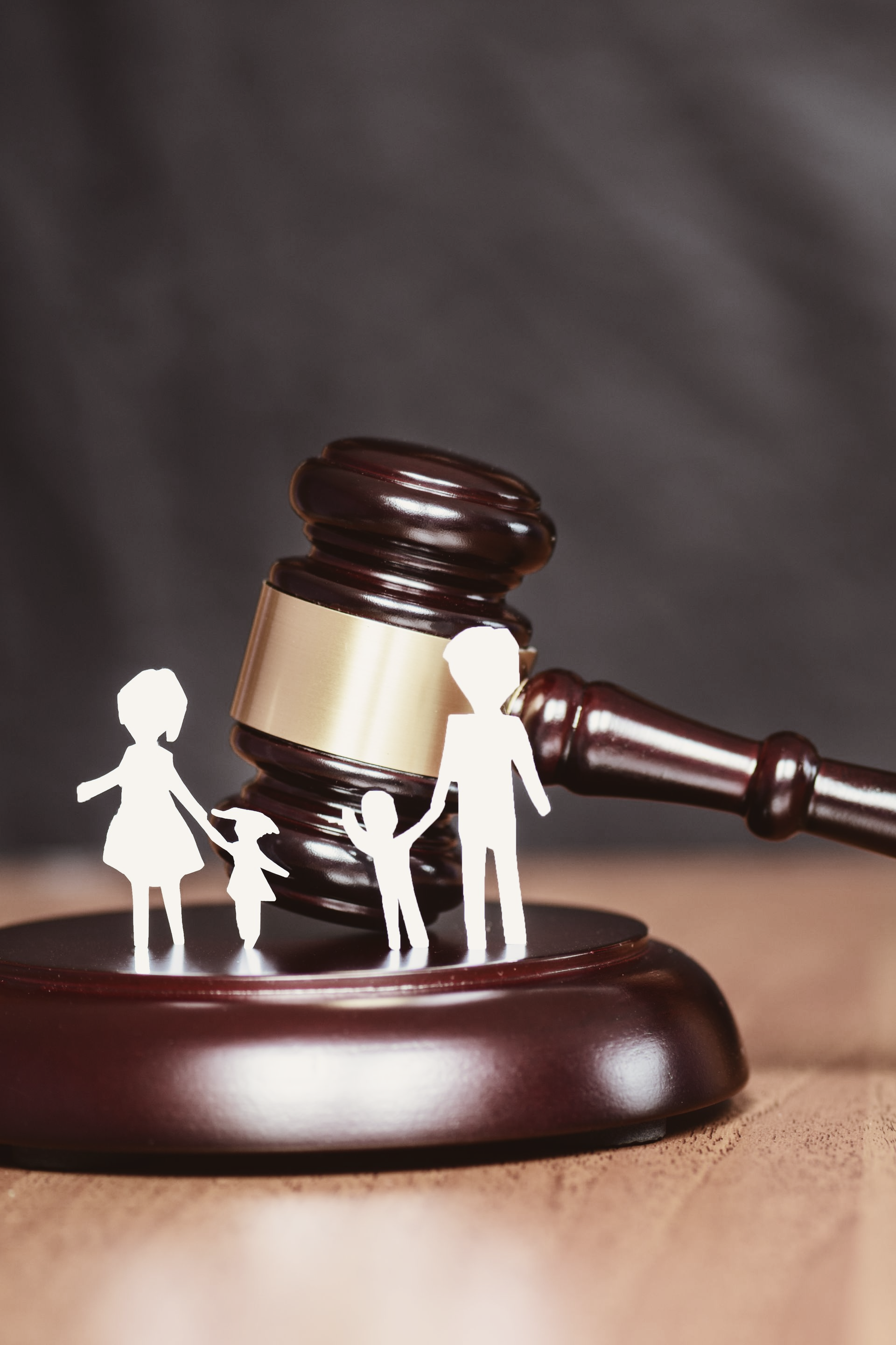 Maillet sur bloc de bois avec des figures familiales découpées en papier, impliquant des relations juridiques et familiales.