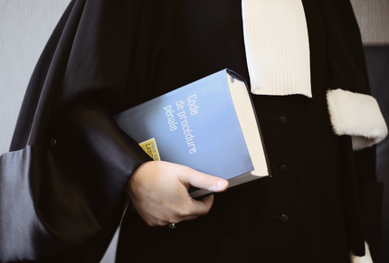 Une personne vêtue d'une robe noire tenant le Code de procédure pénale.