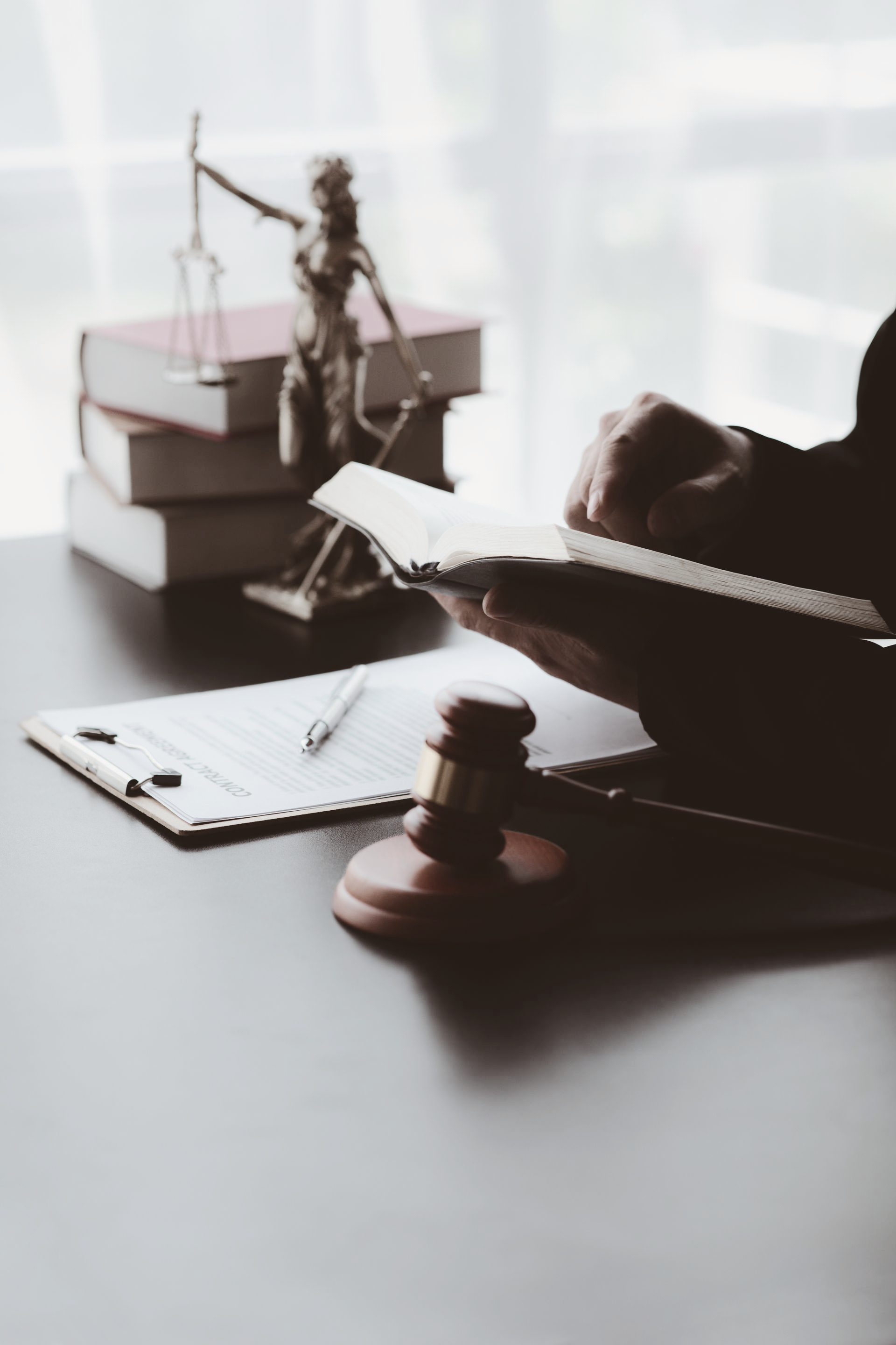 Une personne examinant des documents juridiques avec un marteau, une balance de la Justice et des livres sur un bureau.