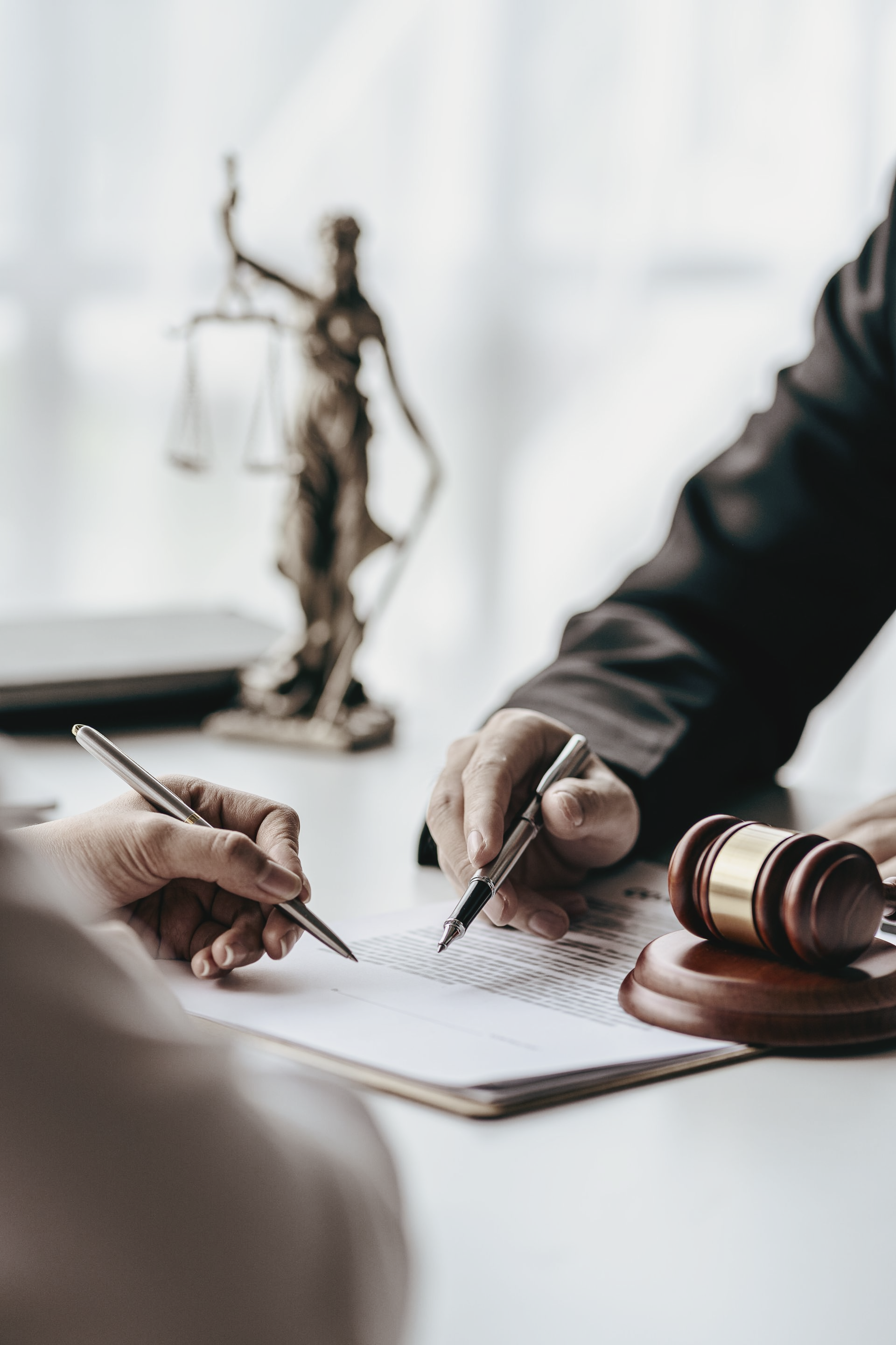 Deux personnes signant des documents à une table avec un marteau, une balance de la Justice et des stylos.