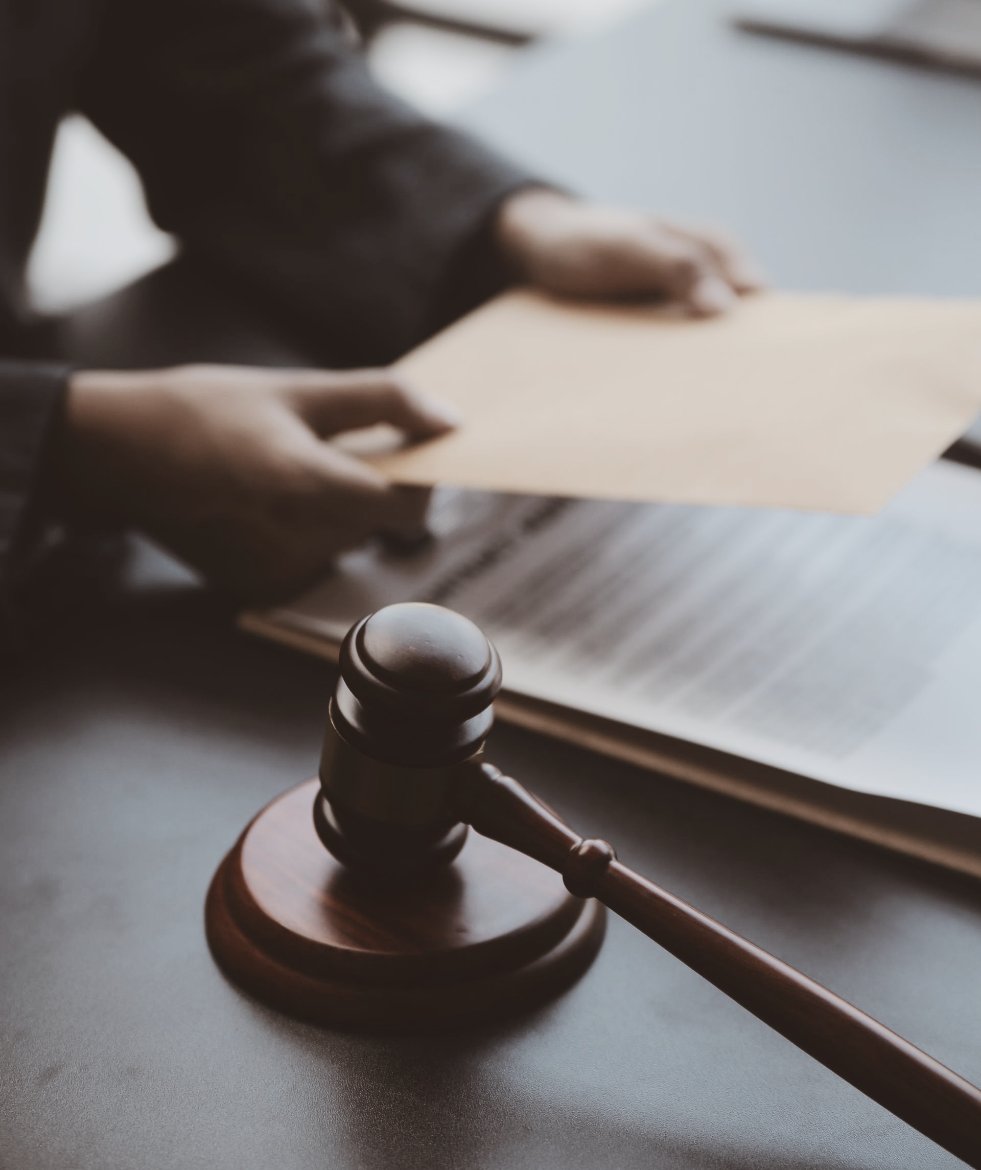 Un marteau et des documents sur une table. Une personne tient des documents.