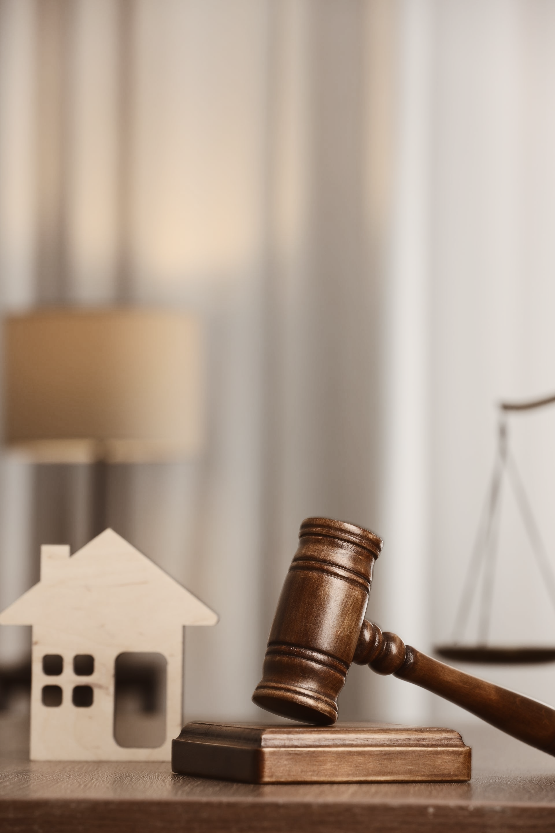 Marteau en bois sur un bloc à côté d'une petite découpe de maison et d'une balance, suggérant une vente aux enchères immobilière.