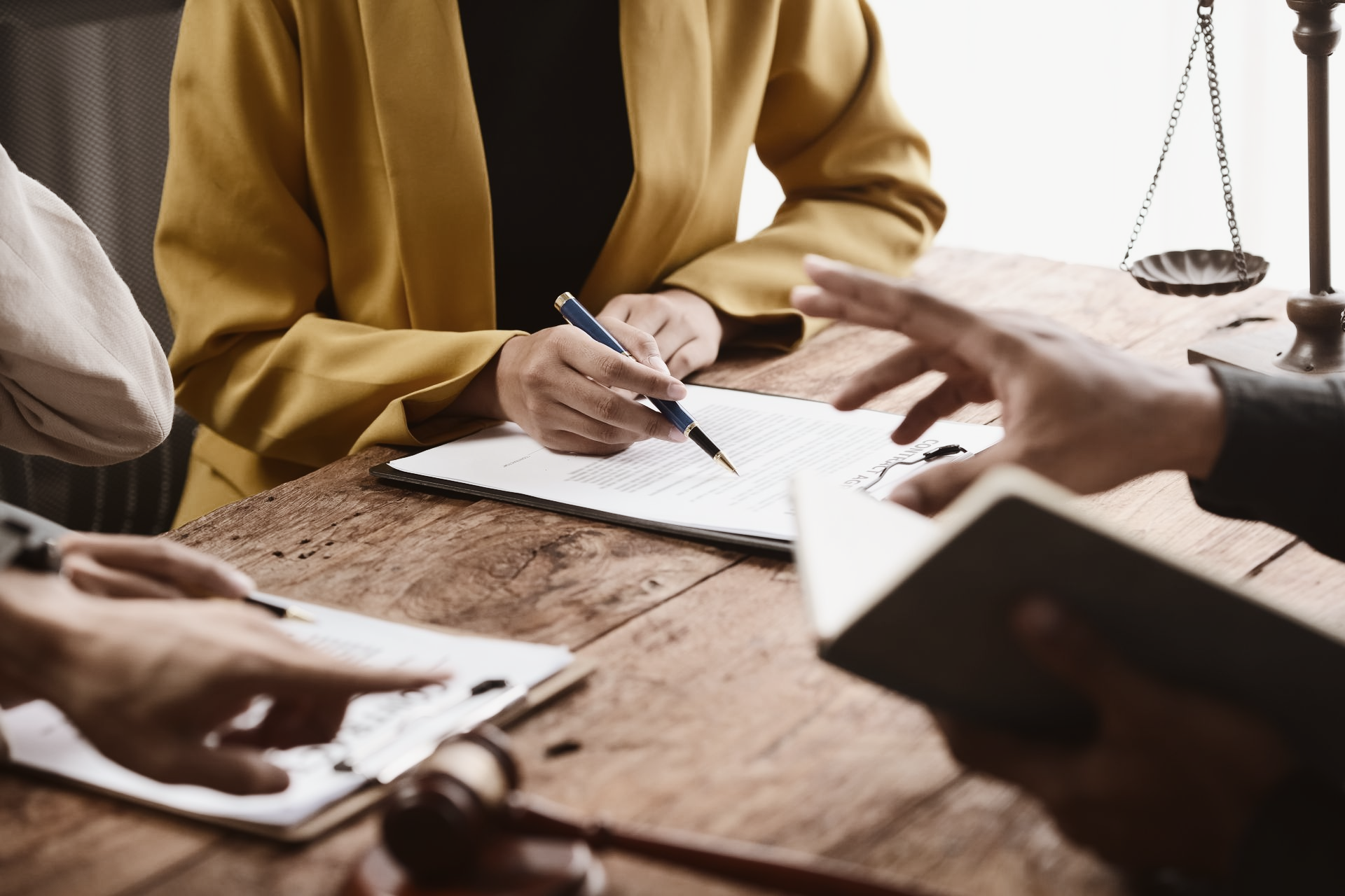 Des gens en discussion, avec des documents juridiques, une balance et un marteau sur une table en bois.