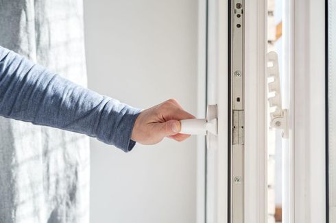 Girando a mano una manija blanca en un marco de ventana parcialmente abierto.