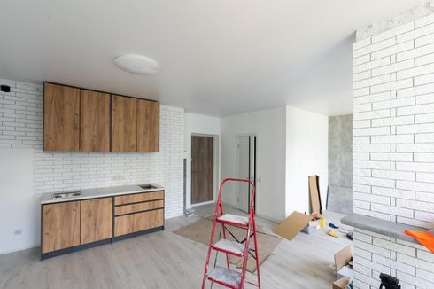 Renovación de cocina con paredes de ladrillo blanco, armarios de madera, escalera roja y herramientas en el suelo.