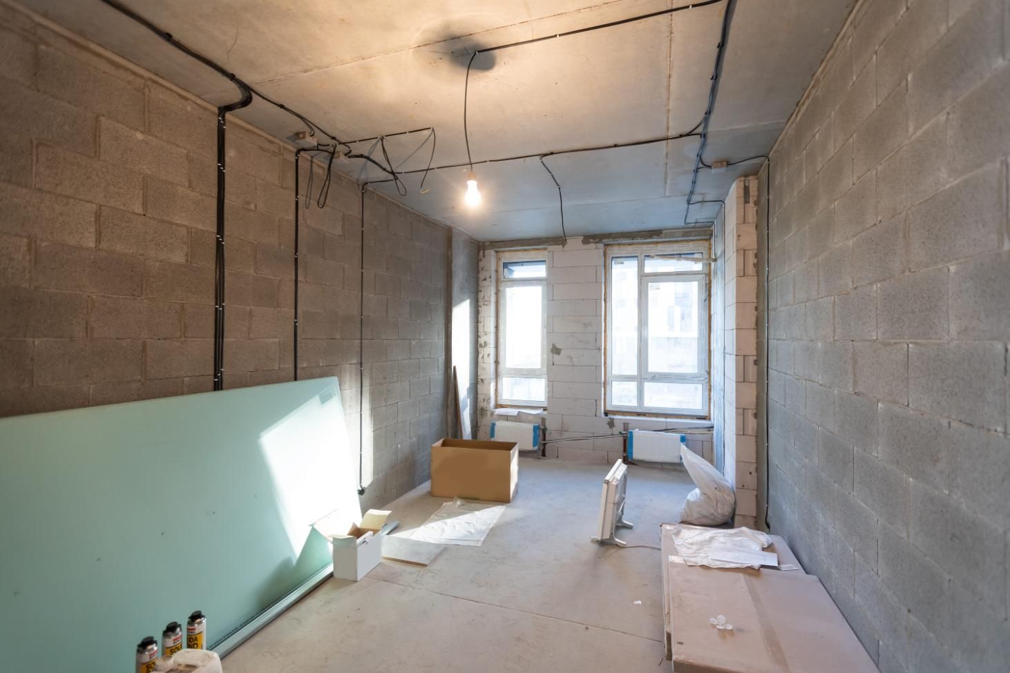 Habitación sin terminar con paredes de bloques de hormigón, cableado a la vista y materiales de construcción en el suelo.
