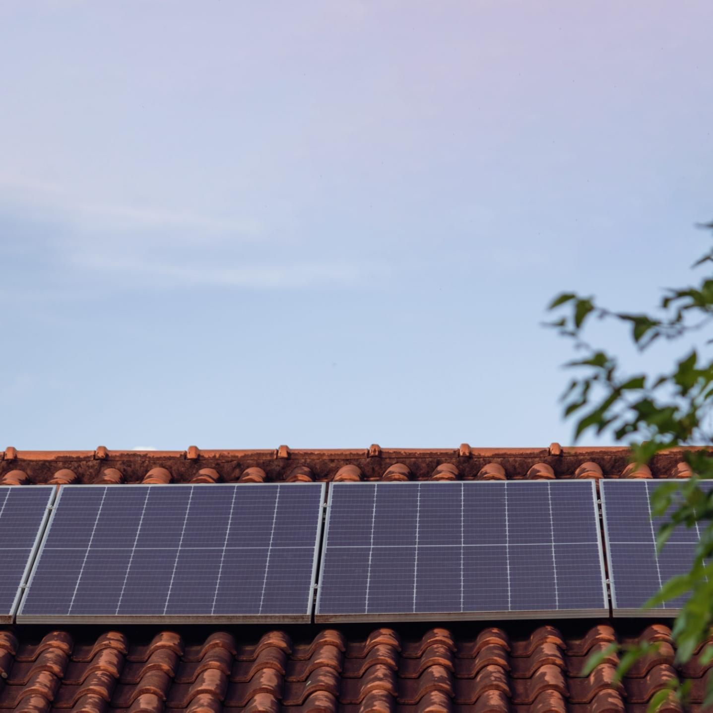 Paneles solares en un tejado de tejas rojas bajo un cielo azul despejado.