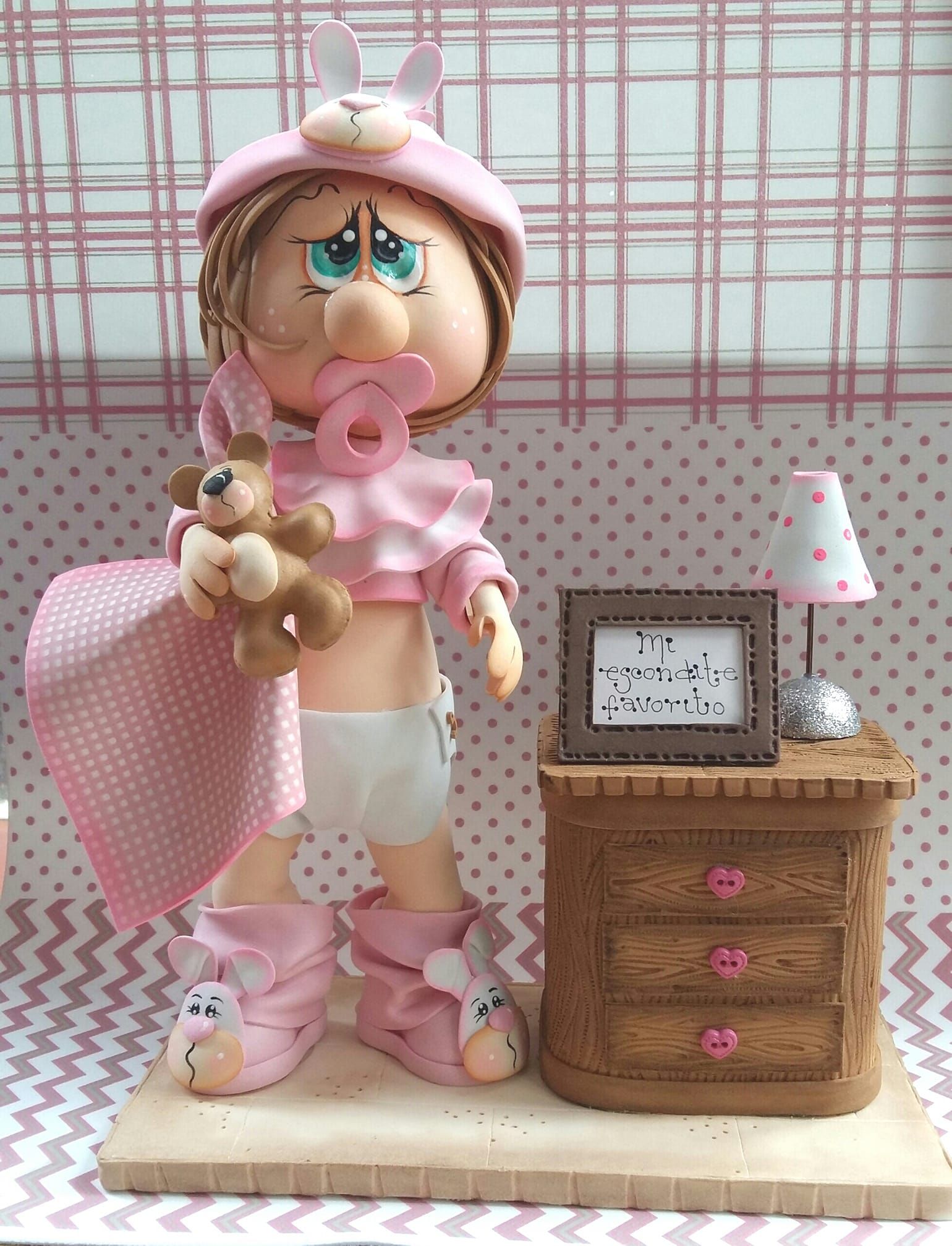 Una figura de una niña sosteniendo un osito de peluche junto a una mesita de noche.
