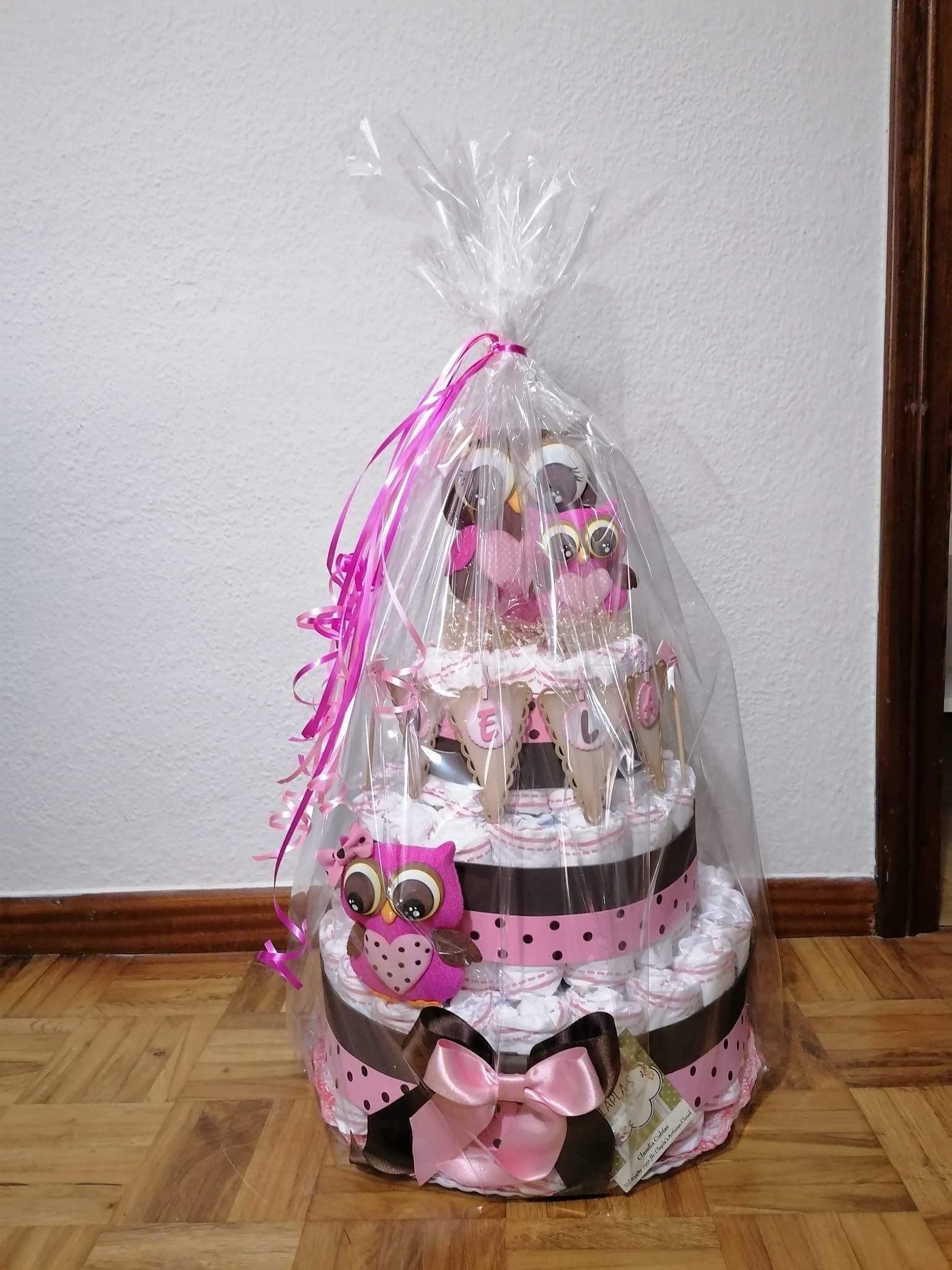 Una torta de pañales está envuelta en plástico y colocada sobre un piso de madera.