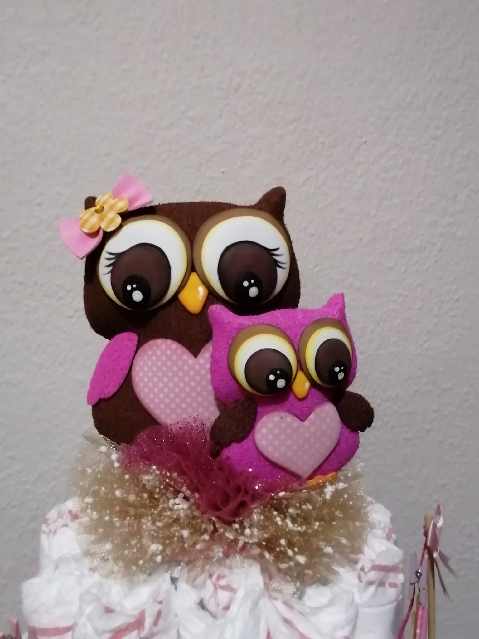 Dos búhos de peluche están sentados encima de un pastel de pañales.