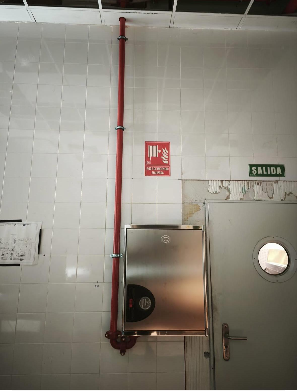 Cocina comercial con estufa de acero inoxidable, campana extractora y extintor rojo en la pared.