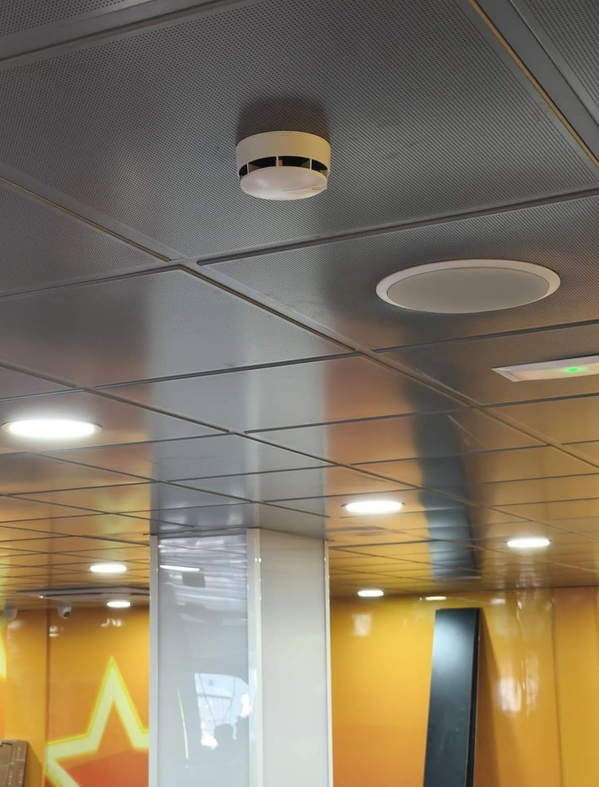 Techo en una habitación moderna con luces empotradas, rejillas de ventilación y paredes amarillas con un brillo de estrella de neón.