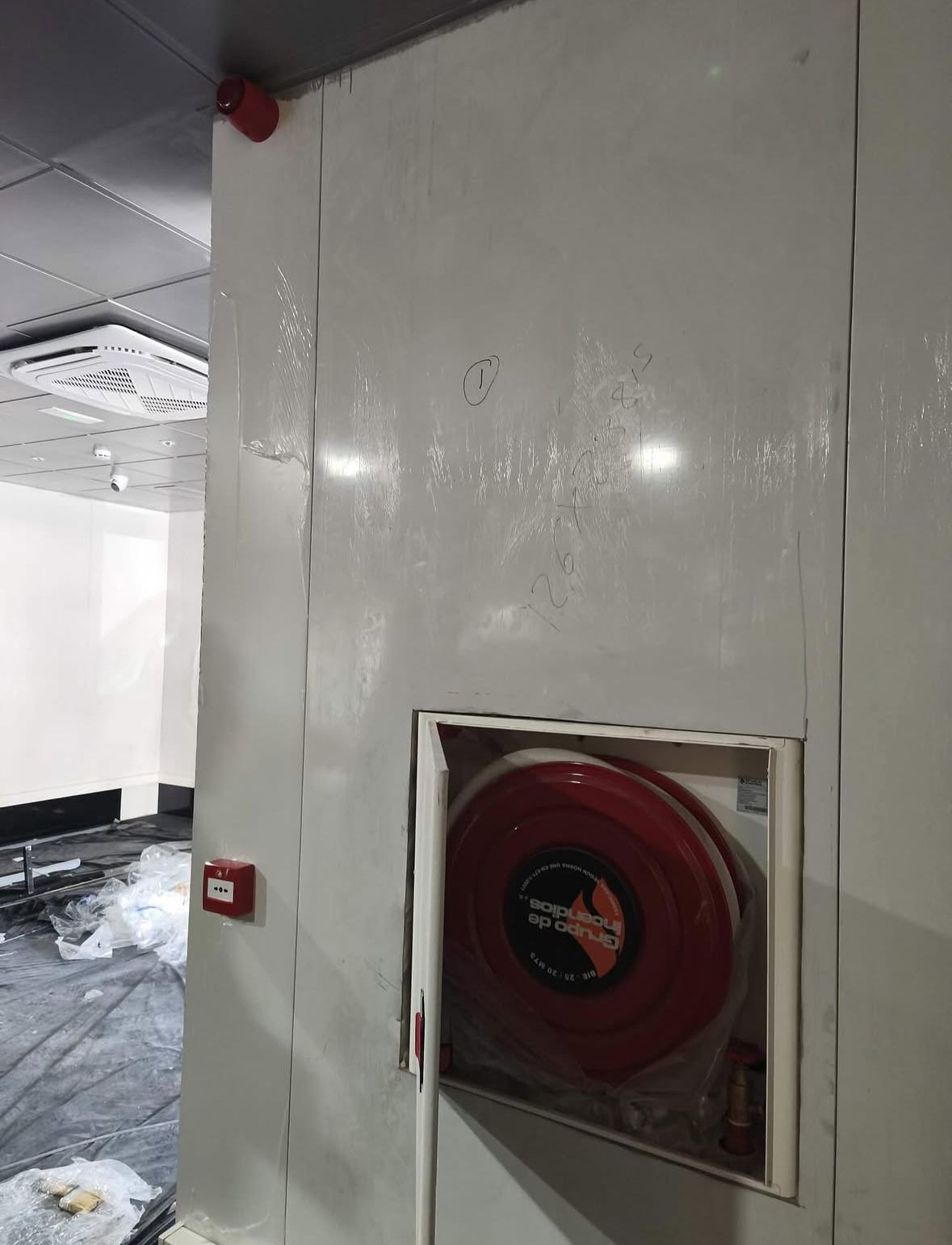 Una manguera contra incendios de color rojo está montada en una pared blanca de un pasillo dañado.