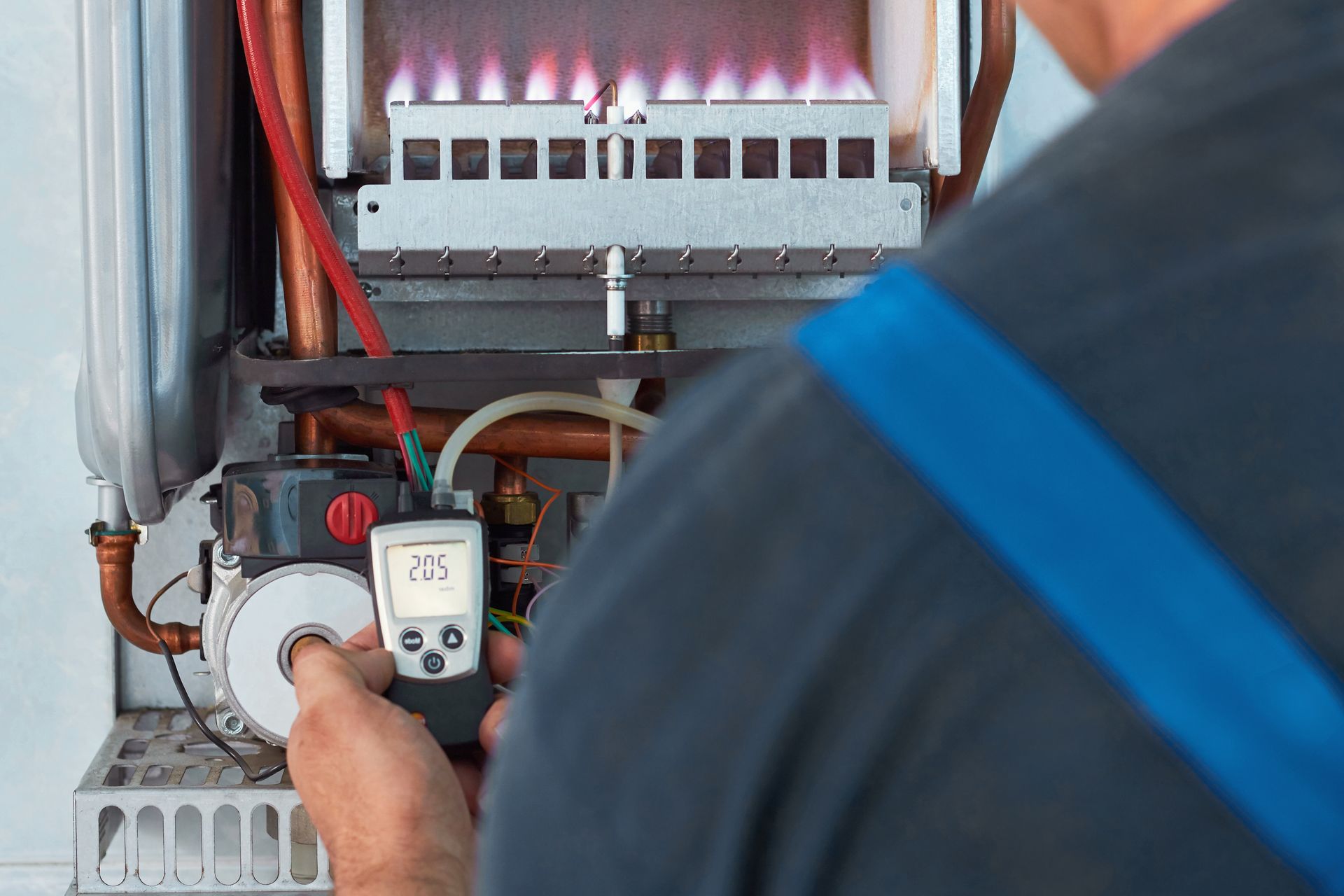 Un technicien utilise un appareil de mesure portatif pour inspecter une chaudière à gaz présentant des flammes bleues visibles.
