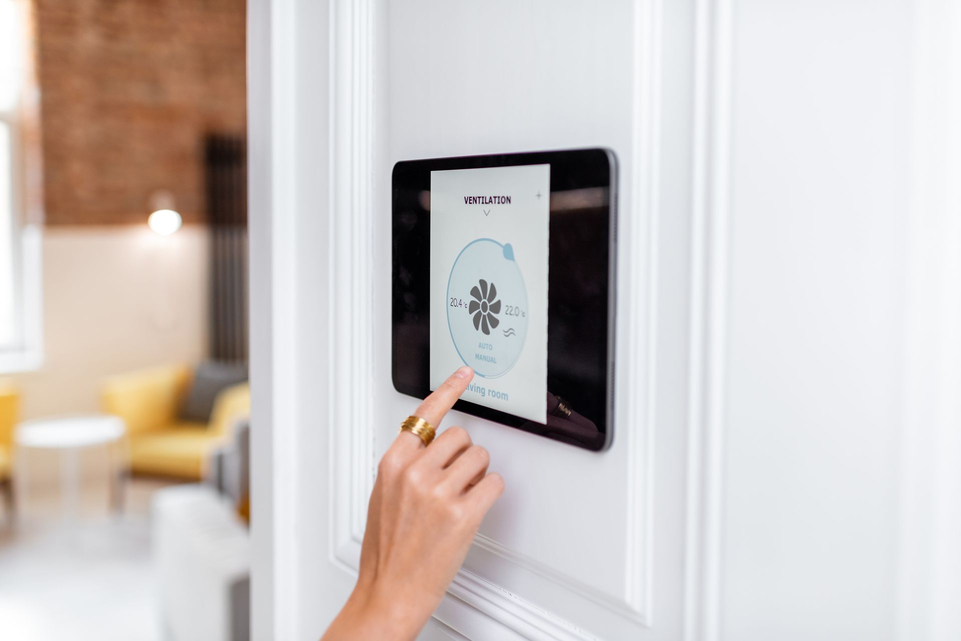 Main touchant un panneau de commande tactile mural dans un intérieur de maison.