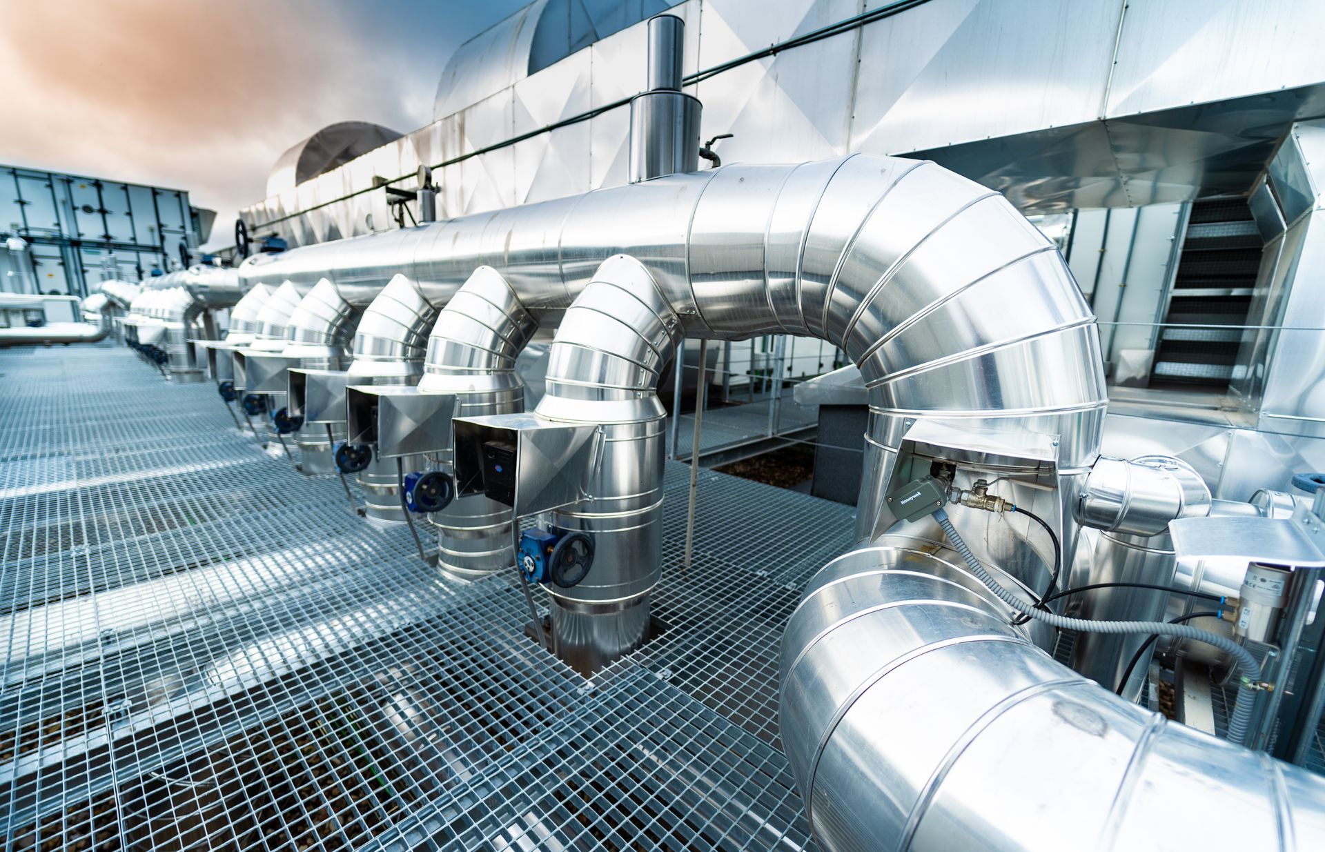 Toit industriel brillant avec de grands conduits de ventilation argentés et une grille métallique.