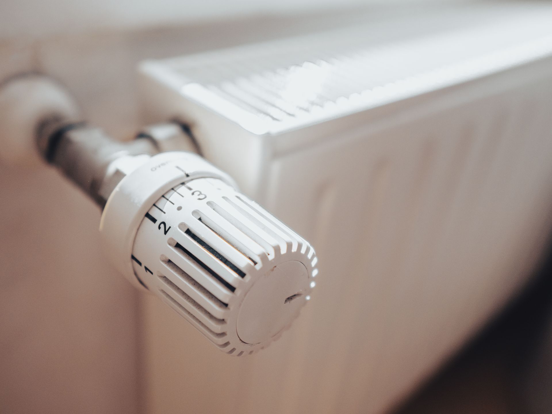 Gros plan sur le bouton blanc d'un thermostat de radiateur, avec un radiateur flou en arrière-plan.