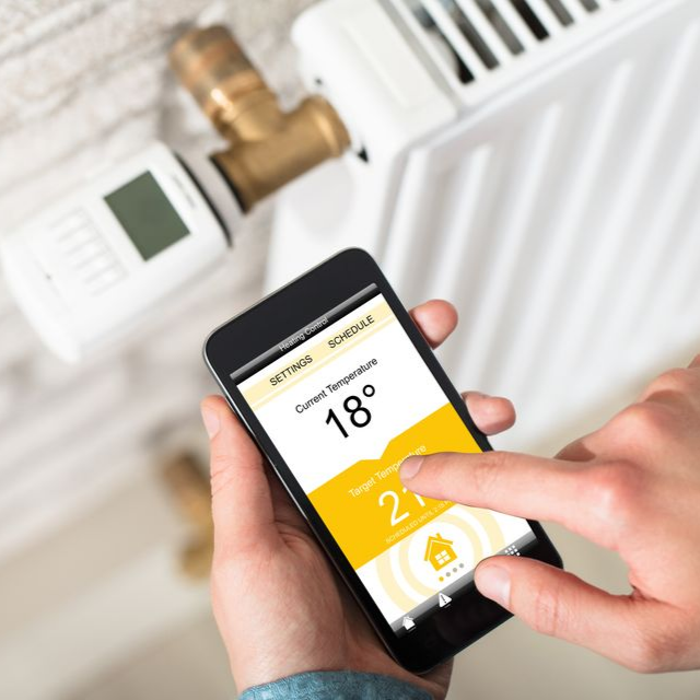 Des mains règlent un thermostat intelligent sur un radiateur, affichant 18°C sur l'écran.