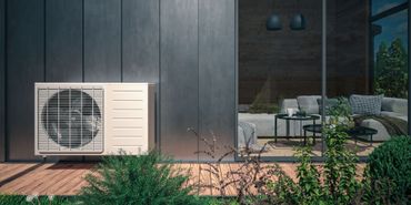 Terrasse extérieure avec un climatiseur blanc à côté d'un revêtement sombre et d'une porte vitrée au crépuscule.