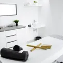 Habitación minimalista blanca con cama, lavabo, escritorio, silla y toallas dobladas, como un spa o una sala de tratamientos.