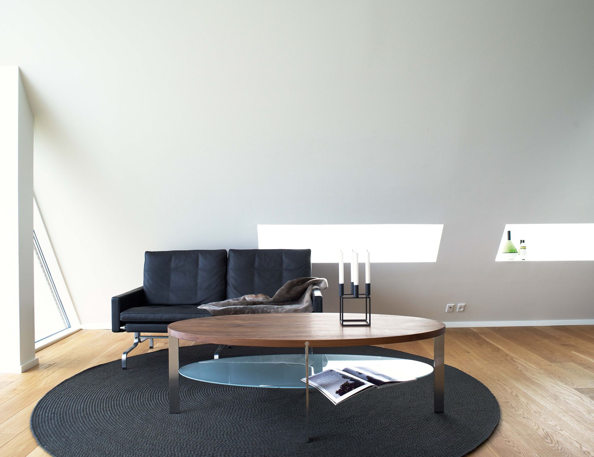 Ovaler Couchtisch mit Glasablage vor einem schwarzen Sofa