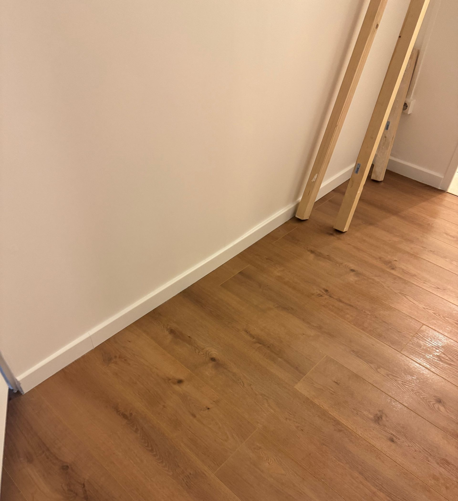 Coin vide avec parquet, mur et planches appuyées près de l’entrée.