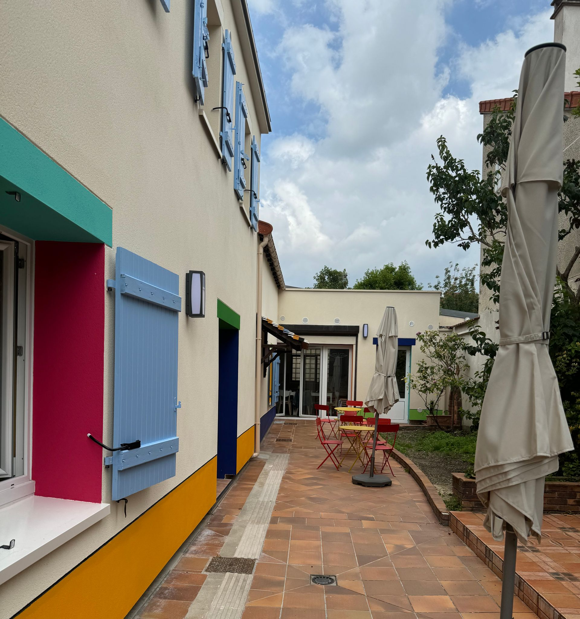 Allée dans une cour, avec du mobilier de terrasse, des parasols et des plantes en pot, à côté d’un bâtiment.
