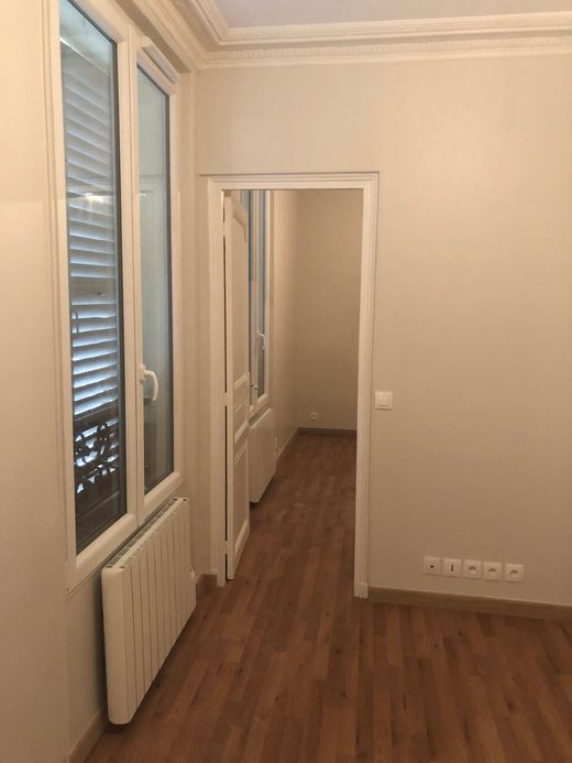 Couloir étroit avec un parquet, des murs, de hautes fenêtres et une porte donnant sur une autre pièce.