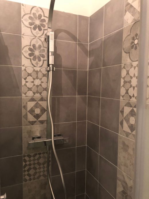 Douche à l’italienne avec douchette à main et carreaux décoratifs à motifs floraux.