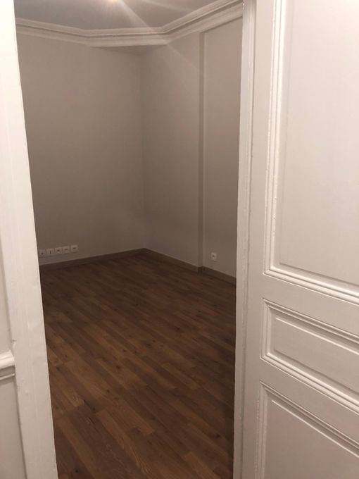 Pièce vide avec des murs à panneaux et un parquet, vue depuis une porte ouverte.