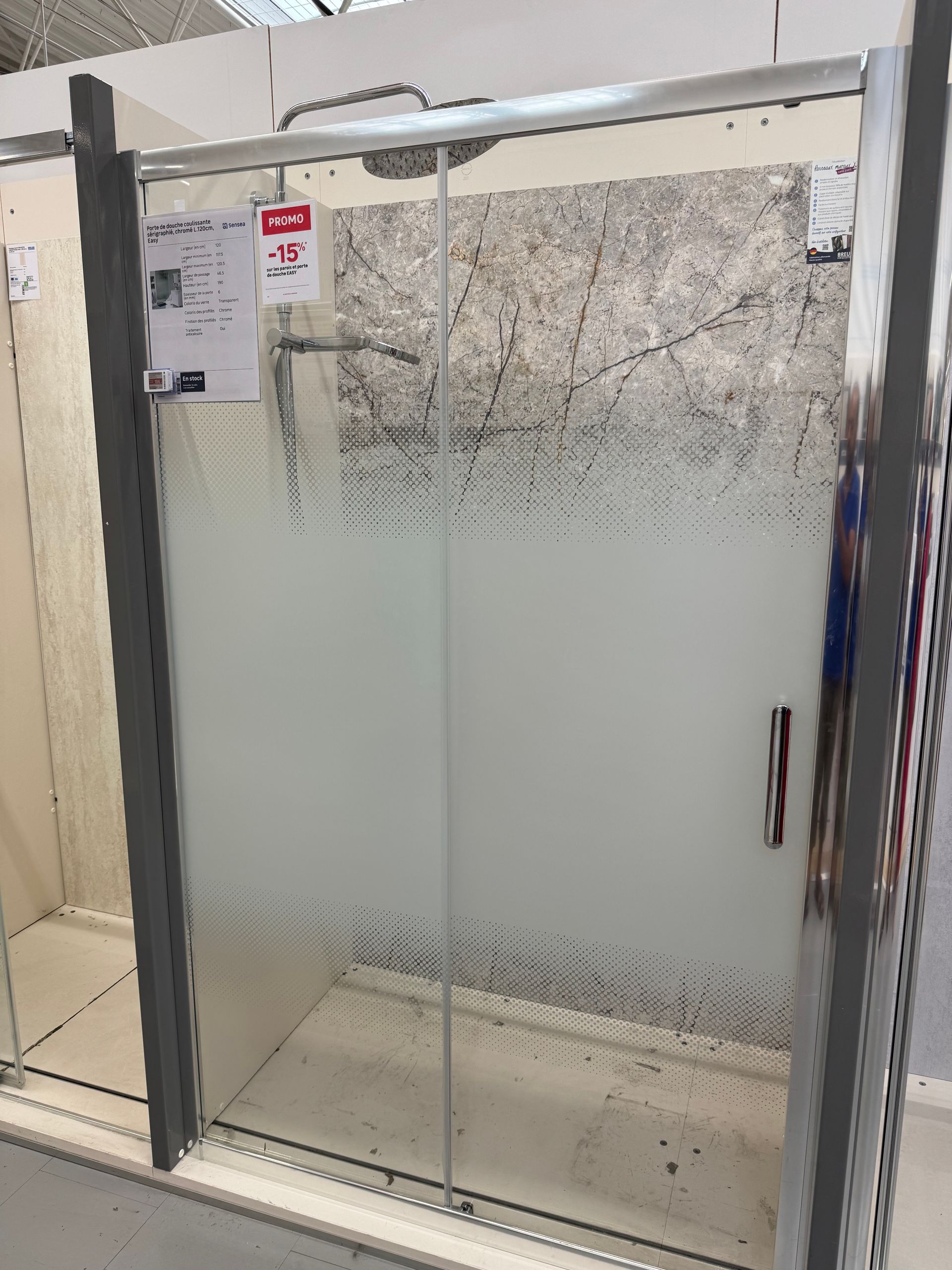 Paroi de douche en verre dépoli avec cadre et poignée chromés dans une salle de bains carrelée.