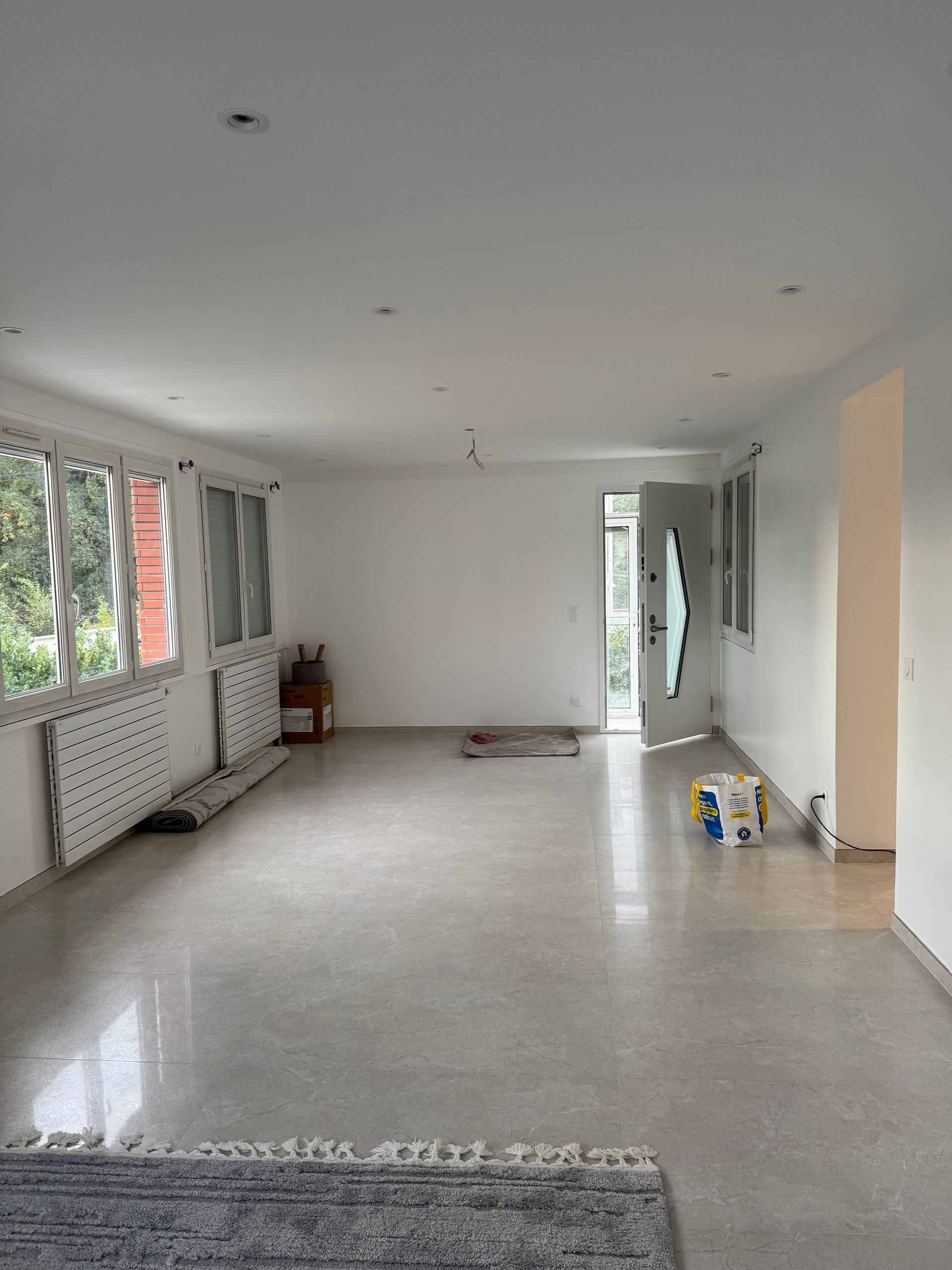 Salon vide et non meublé avec de grandes fenêtres, des murs et un sol carrelé.