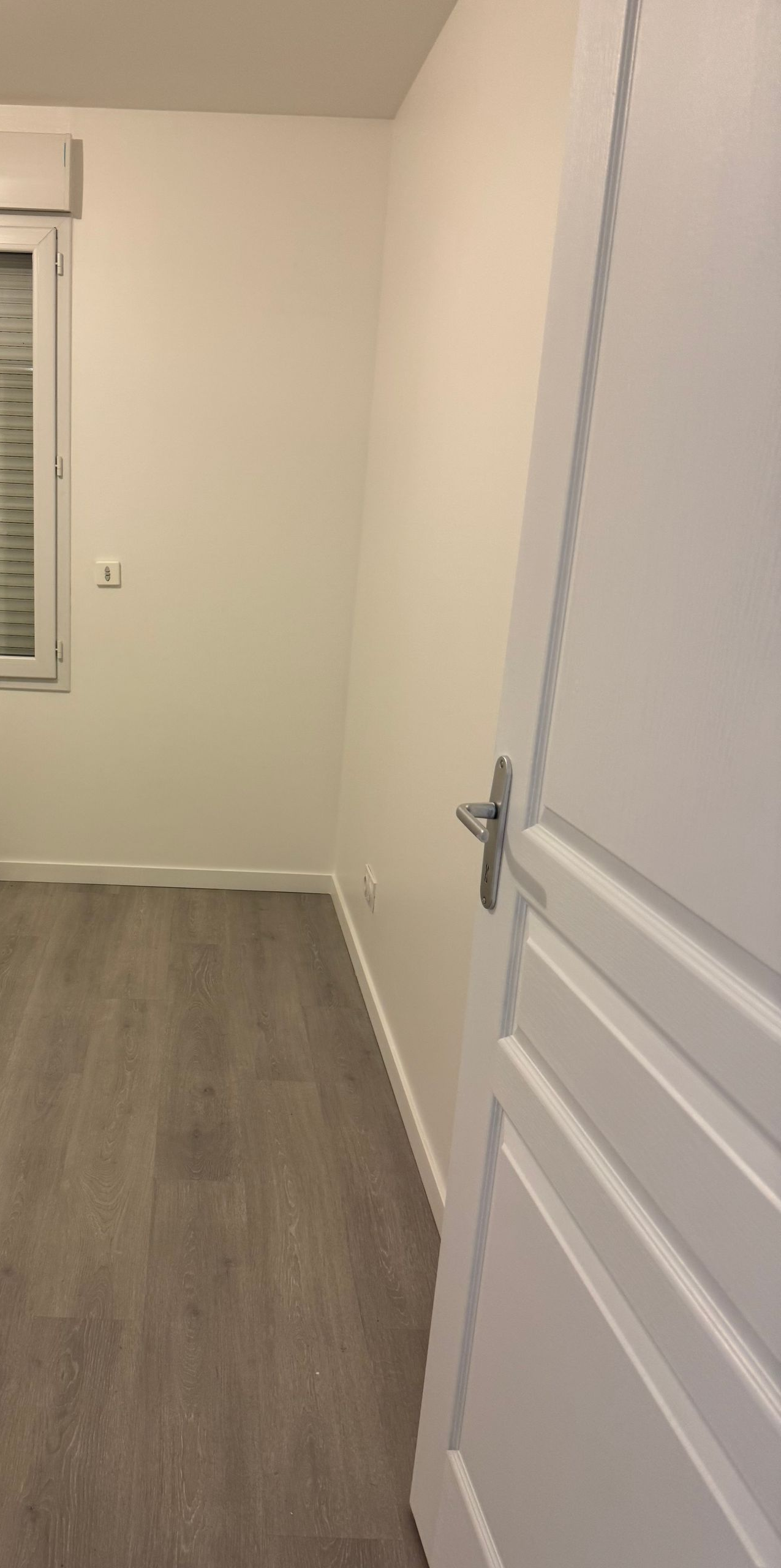 Couloir vide aux murs, avec un parquet et une porte ouverte au premier plan.
