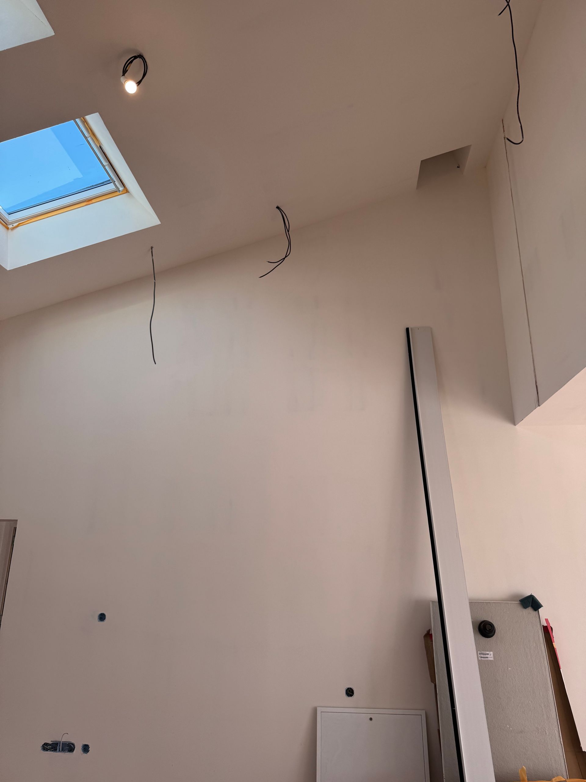 Pièce intérieure avec une lucarne, un haut mur et une porte ou un panneau partiellement installé près du coin.