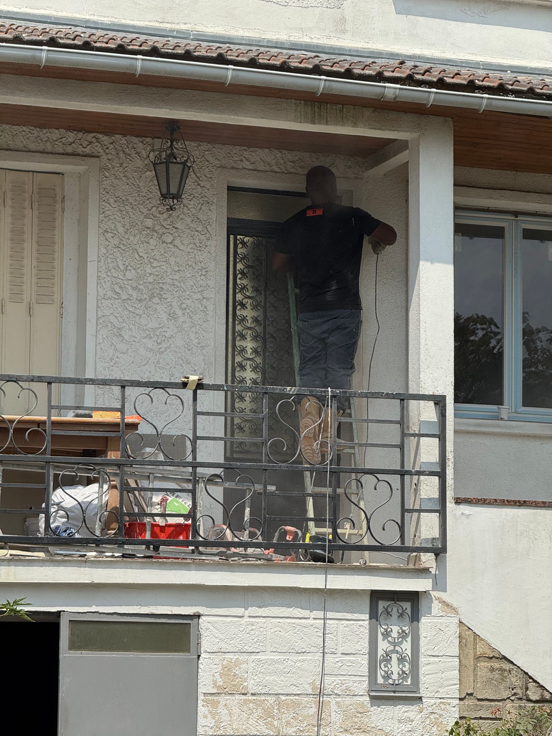 Une personne debout sur un petit balcon, près d’un immeuble d’habitation, en train de travailler sur l’entrée.