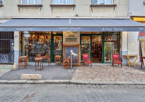 Quelques meubles et un tableau posé dans la rue devant la façade d'une brocante.
