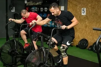 Zona de entrenamiento de fuerza muy concurrida, con gente levantando pesas y usando máquinas de ejercicio.