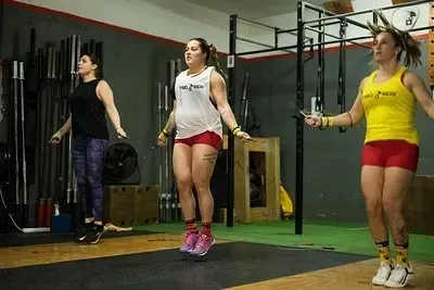 Entrenador guiando a un cliente en un gimnasio junto a pesas rusas y aparatos de entrenamiento.