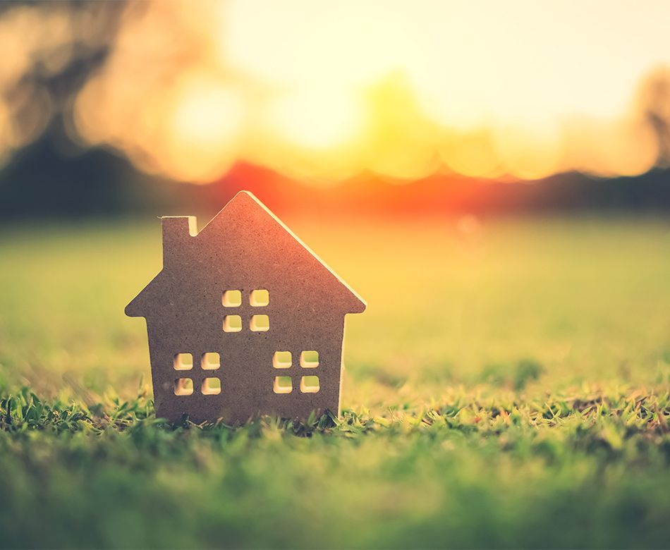 Découpe en bois du profil d'une maison posée dans l'herbe au soleil couchant