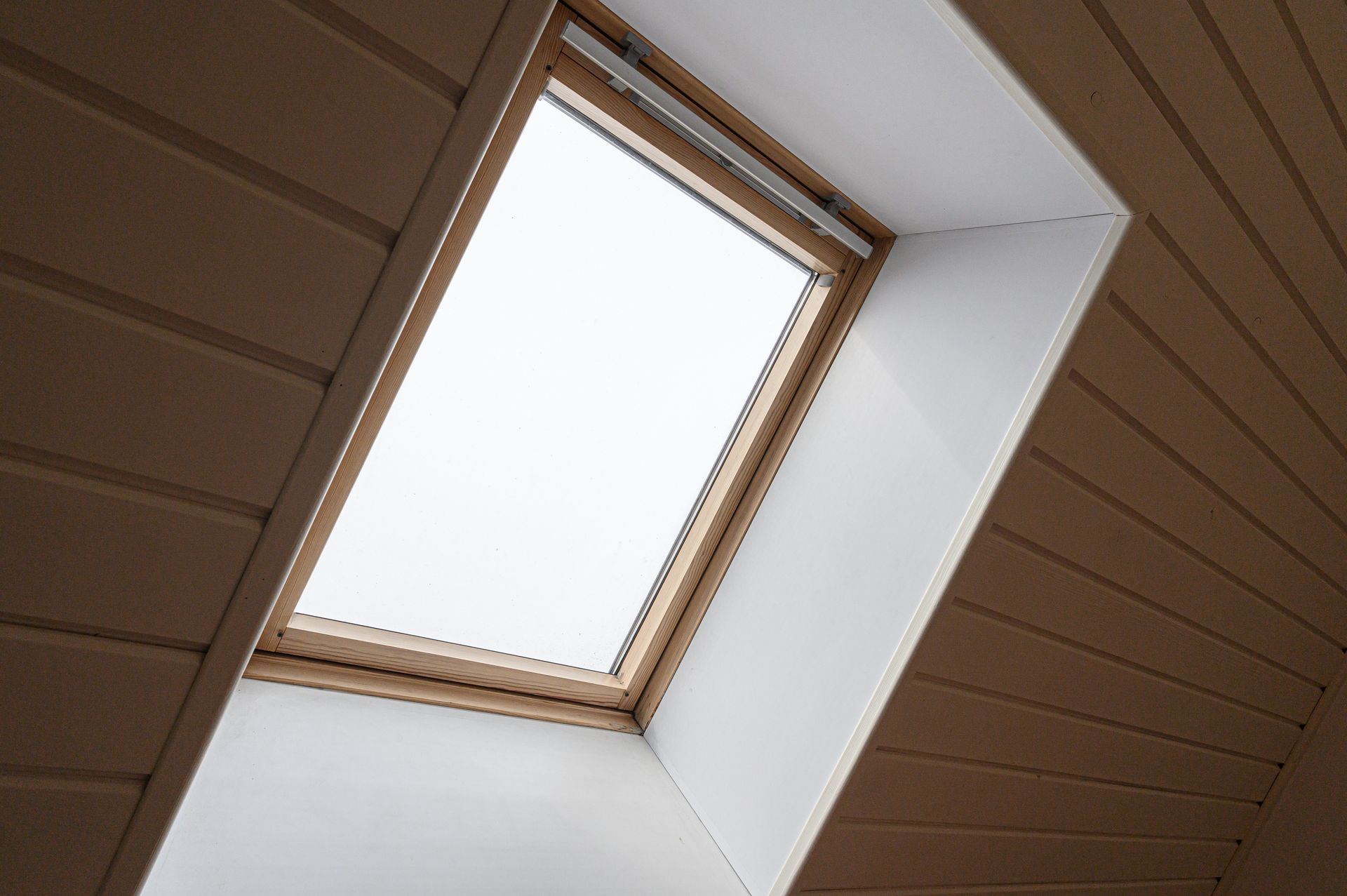 Puits de lumière dans un plafond incliné avec lambris en bois brun et moulures blanches autour de l'ouverture.