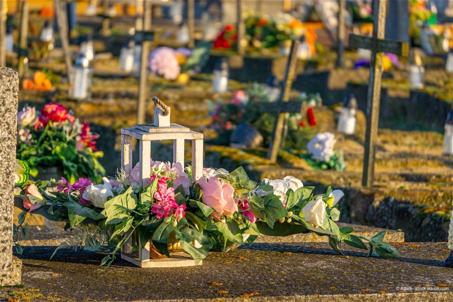 Grab mit weißer Laterne und Blumenarrangement aus rosa und weißen Rosen auf einem Friedhof