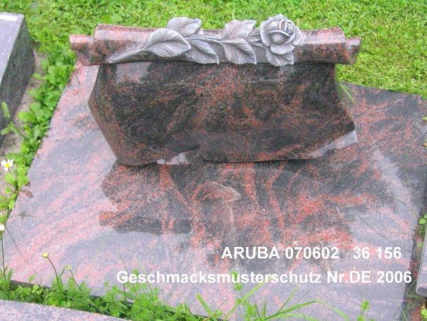 Rötlicher Grabstein mit floraler Verzierung und geschwungenen Linien auf der Oberseite.