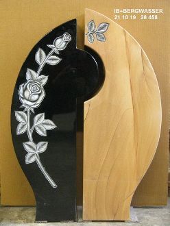 Grabstein mit schwarzem Granit und eingravierter Rosenranke neben hellem Holz mit eingraviertem Blatt 