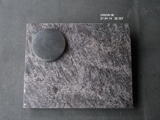 Dunkelgrauer, quadratischer Grabstein mit kreisrundem, erhabenen Element auf der Fläche.