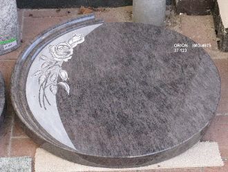 Halbrunder Grabstein mit grauer Maserung und weißem Rosenmotiv auf der linken Seite.