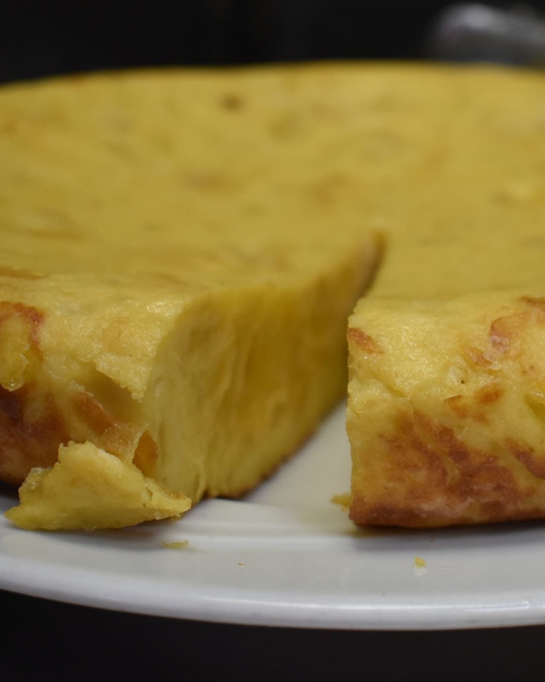 Una tortilla con una rebanada quitada está en un plato blanco.